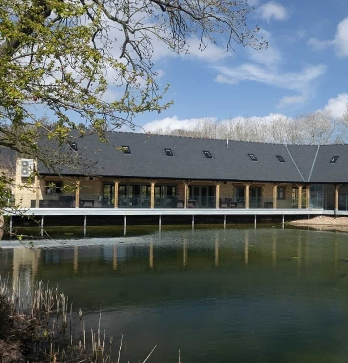 Blisworth building with a pond and trees under a blue sky.